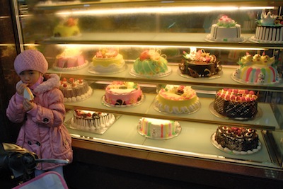 photo d'une jeune fille dégustant un gâteau devant une vitrine de patisserie